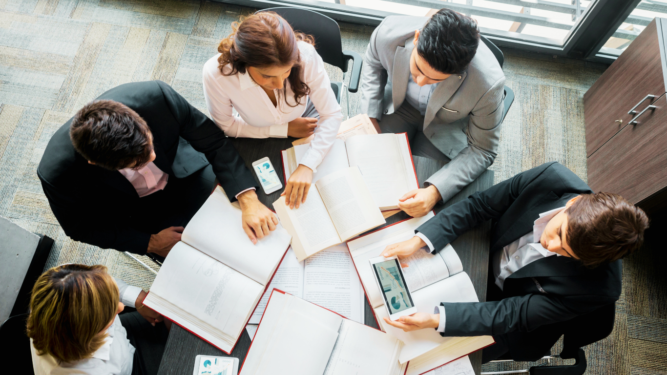 A group of professionals collaborating over open books and digital tablets in a modern office setting, representing the power of integrated solutions for streamlined business operations.