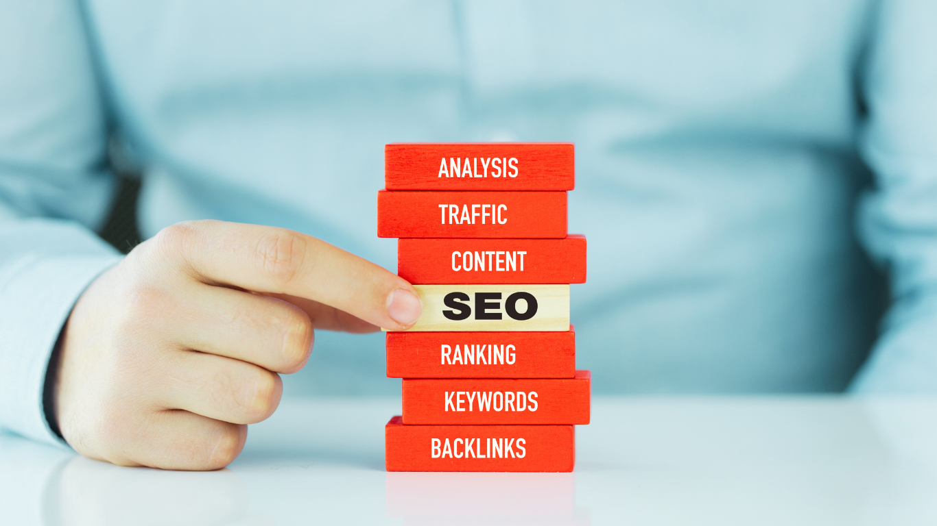 Person’s hand pulling a block labeled “SEO” from a stack of red blocks, each with digital marketing terms like analysis, traffic, content, ranking, keywords, and backlinks.