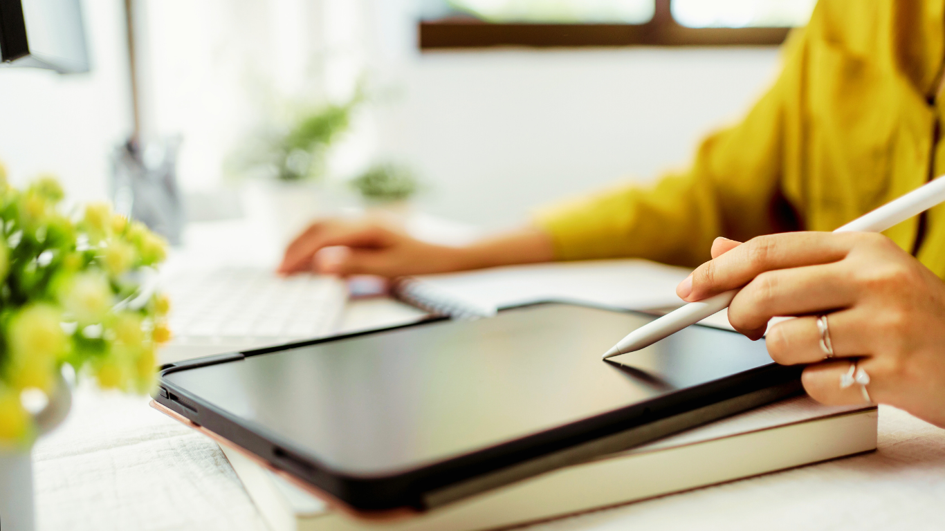 A person using a stylus on a tablet while working at a desk, illustrating the use of digital tools to boost productivity and streamline business tasks.