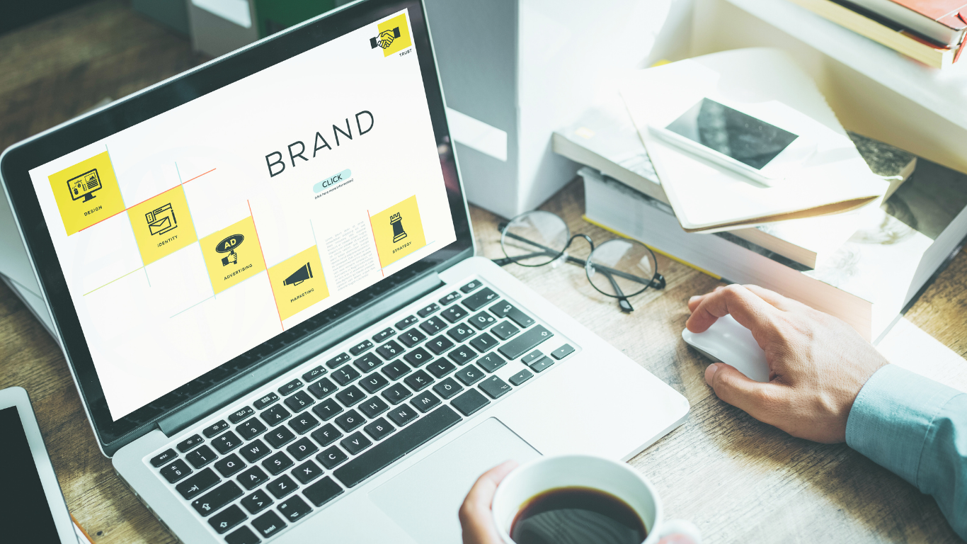 Strategies for Building a Strong Brand Identity Online A person working on a laptop with a digital screen displaying design elements and strategy keywords related to building a strong brand identity online.